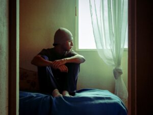 Adolescente sentado en su cama mirando por la ventana en un cuarto en penumbra, imagen que ilustra el aislamiento en la adolescencia